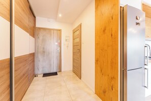 A hallway with a wooden door, a refrigerator, and a tiled floor. - Paryska Deluxe Apartment (Kołobrzeg)