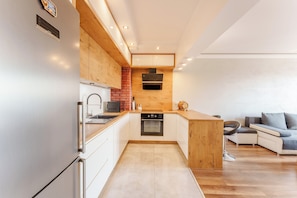 A modern kitchen with a built-in oven, a refrigerator, and a wooden island. - Paryska Deluxe Apartment (Kołobrzeg)