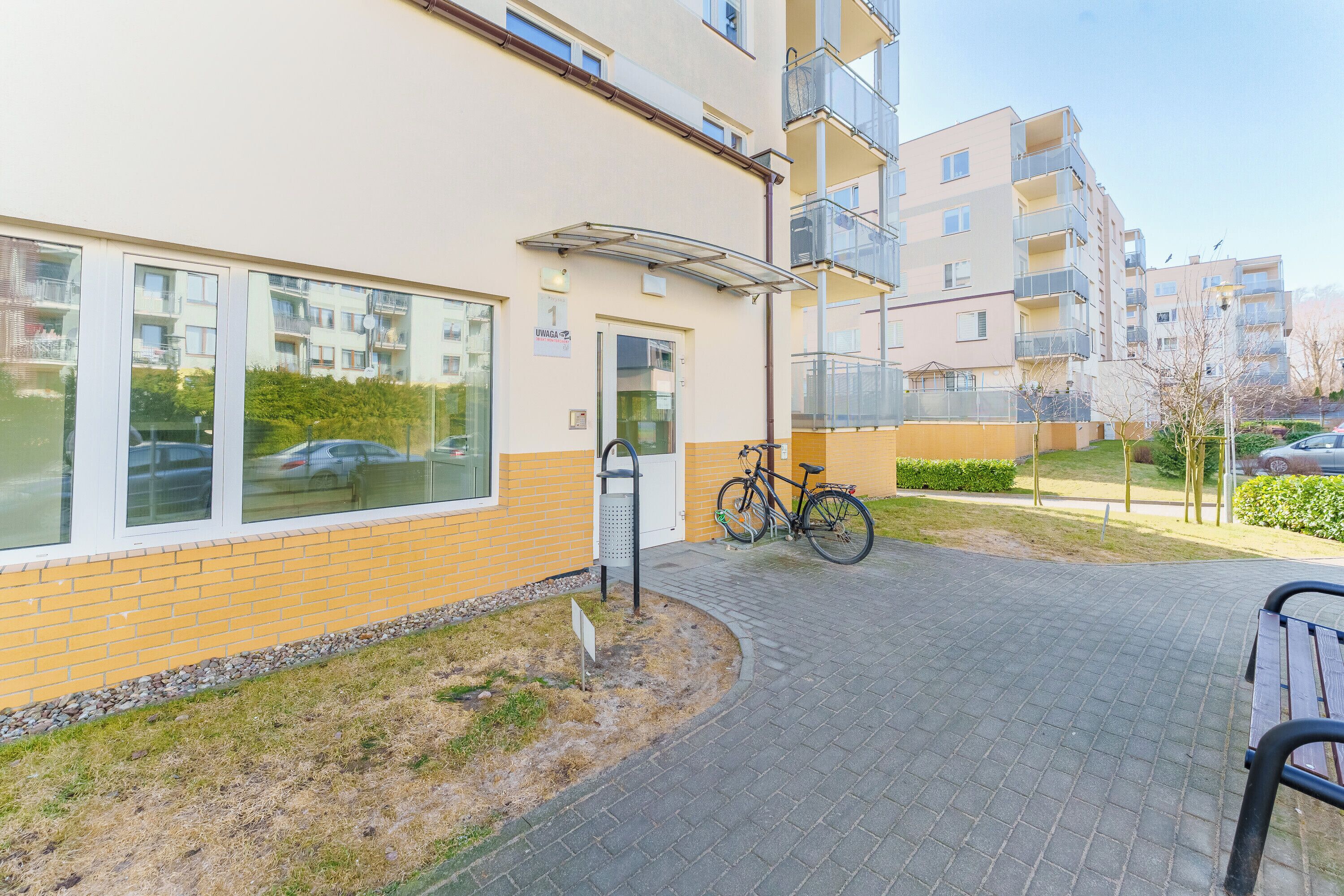 A building with a yellow brick facade, a bicycle parked outside, and a paved walkway.
