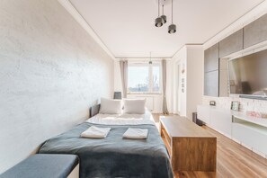 A modern bedroom with a bed, bedside tables, a TV, and a window. - Paryska Deluxe Apartment (Kołobrzeg)