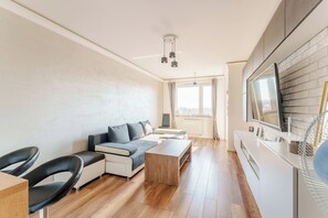 A modern living room with a sofa, coffee table, and chairs. There is a large window providing natural light and a view of the outdoors. - Paryska Deluxe Apartment (Kołobrzeg)