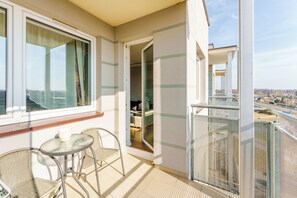 A balcony with a table and chairs, a view of the city, and a door leading to an interior room. - Paryska Deluxe Apartment (Kołobrzeg)