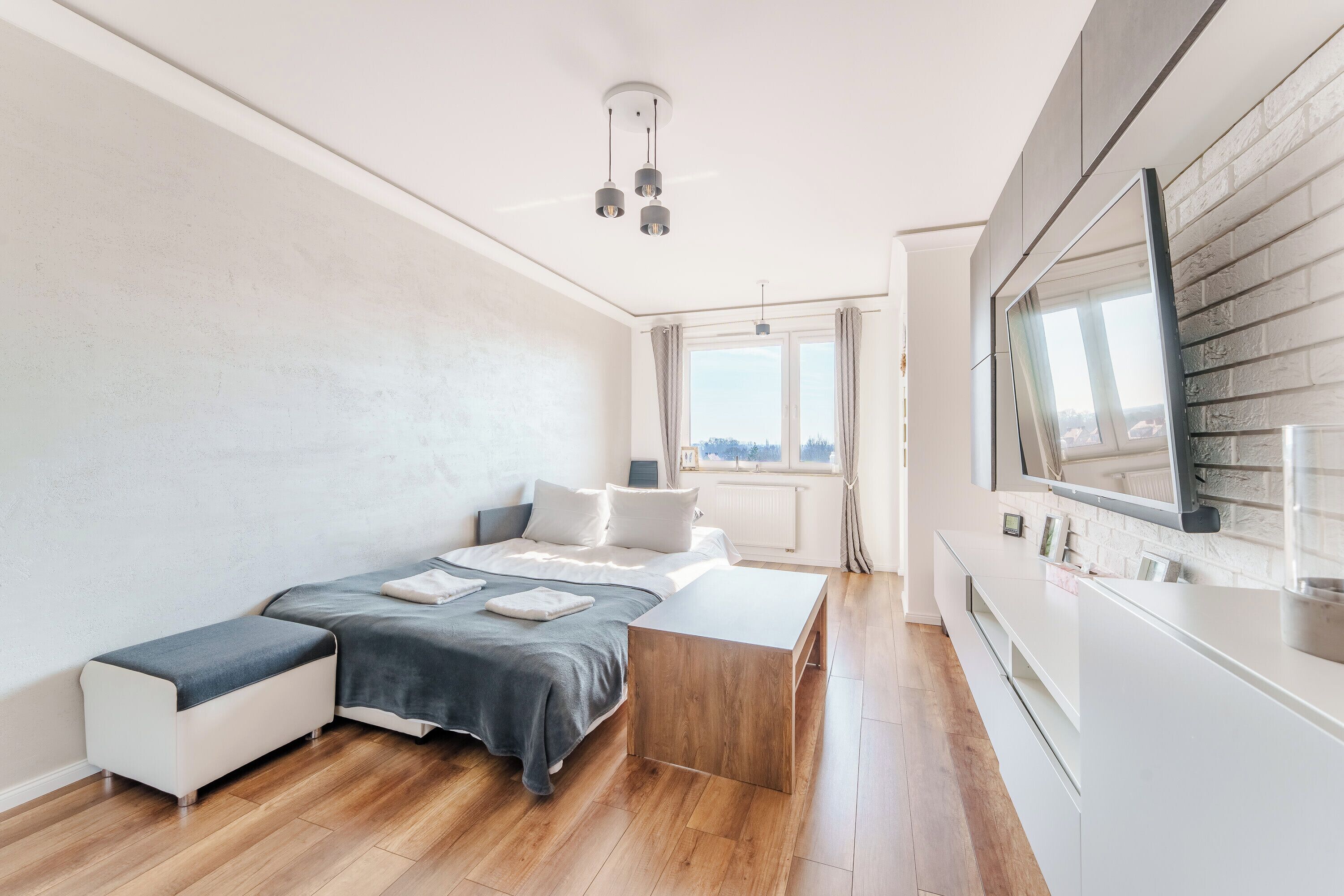 A modern bedroom with a bed, bedside tables, and a view of the city through a window.