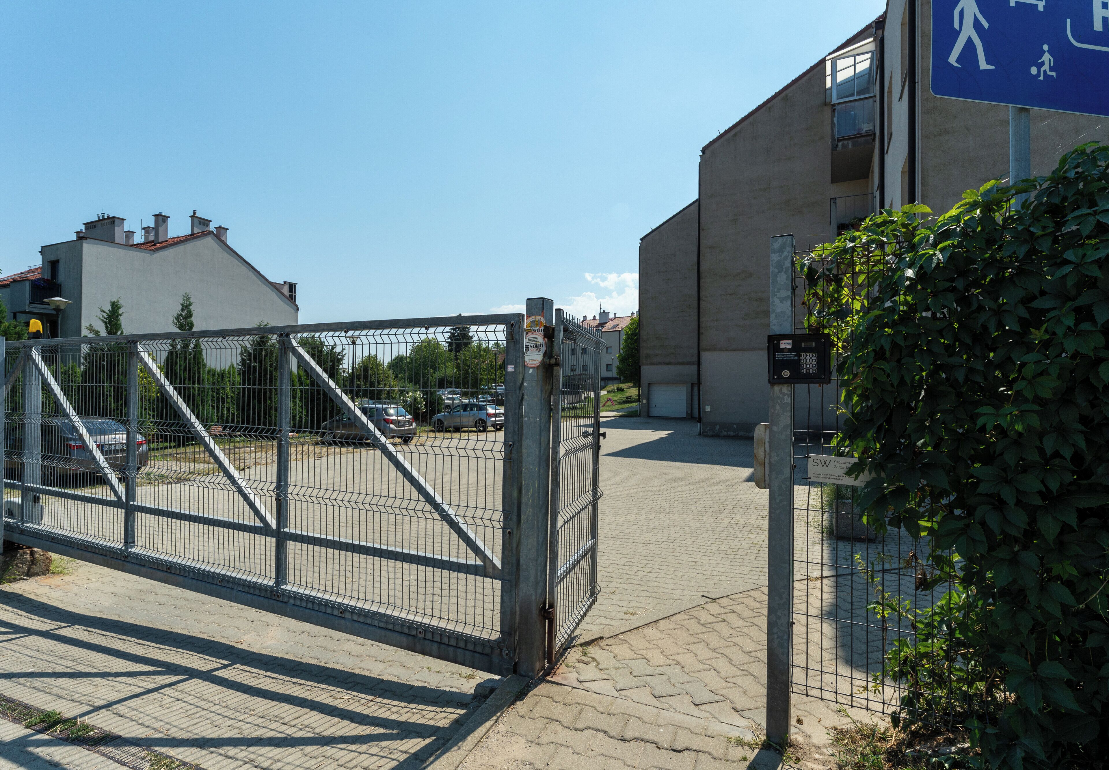 Ingresso recintato di un edificio con vialetto lastricato e auto parcheggiate.