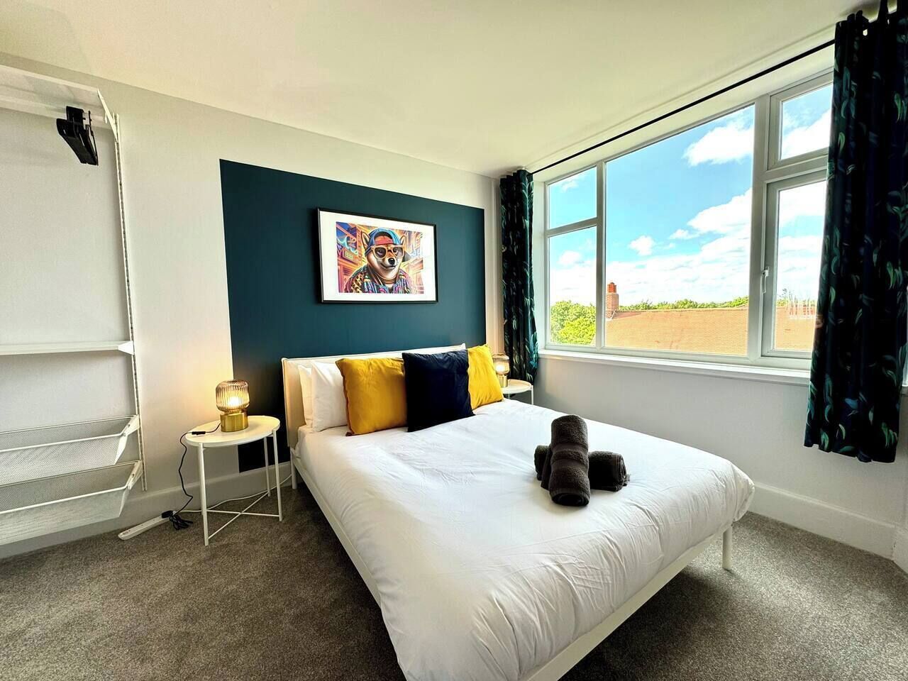 Een hotelkamer met een bed, nachtkastje, lamp, schilderij aan de muur en een raam met gordijnen.