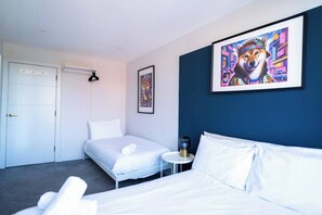 Ein Hotelzimmer mit einem Bett, einem Nachttisch, einem Sessel, einer Tür und zwei gerahmten Bildern an der Wand.
