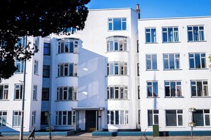 Ein mehrstöckiges Gebäude mit flacher Fassade, großen Fenstern und einem Hauseingang in der Ecke.