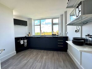 A modern kitchen with a large window, dark cabinetry, and a white countertop. - #142 Bournemouth Flat| Near AlumChine Beach|for 10 (Bournemouth)