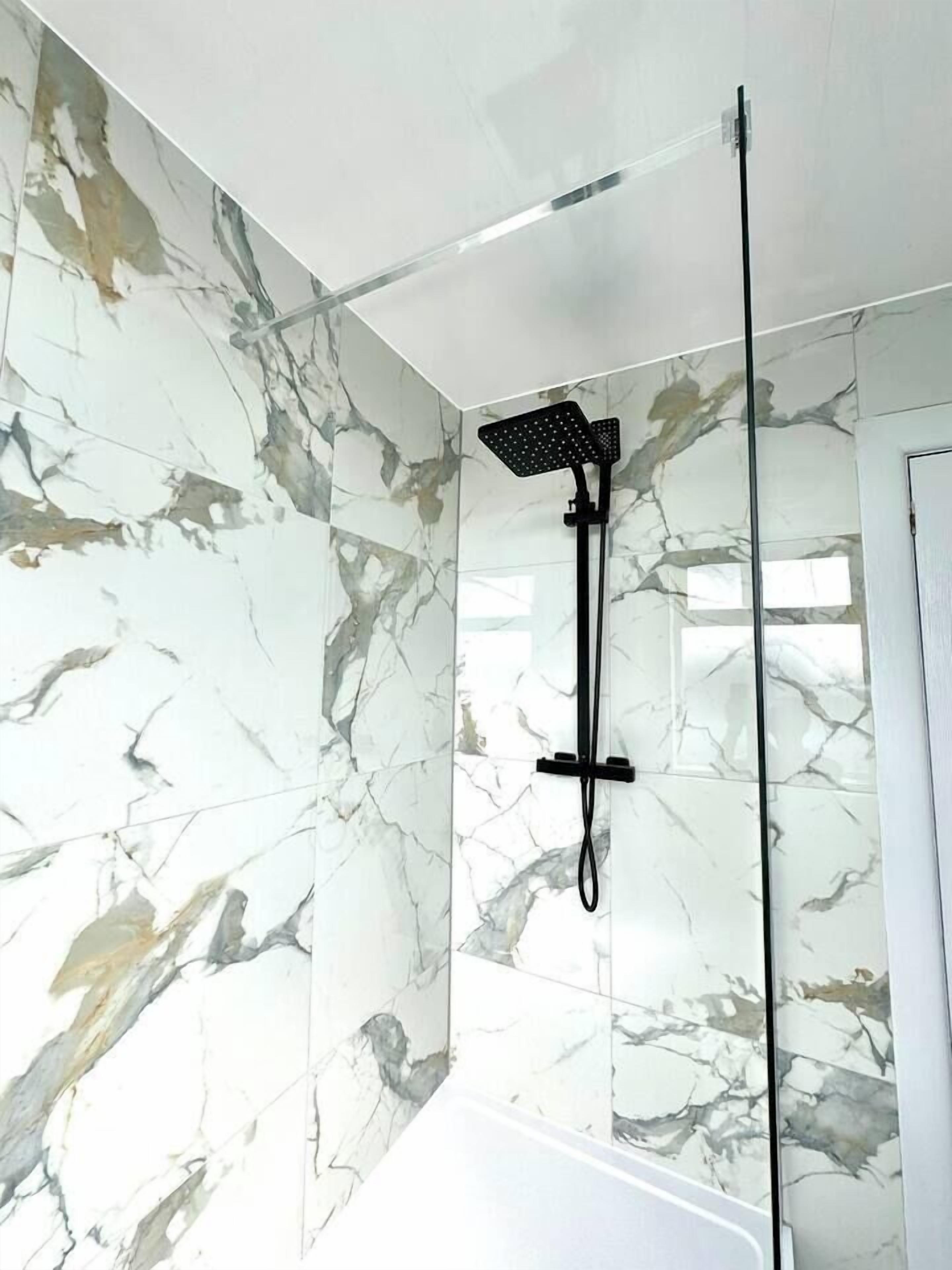A bathroom with a shower enclosure, marble walls, and a white bathtub.