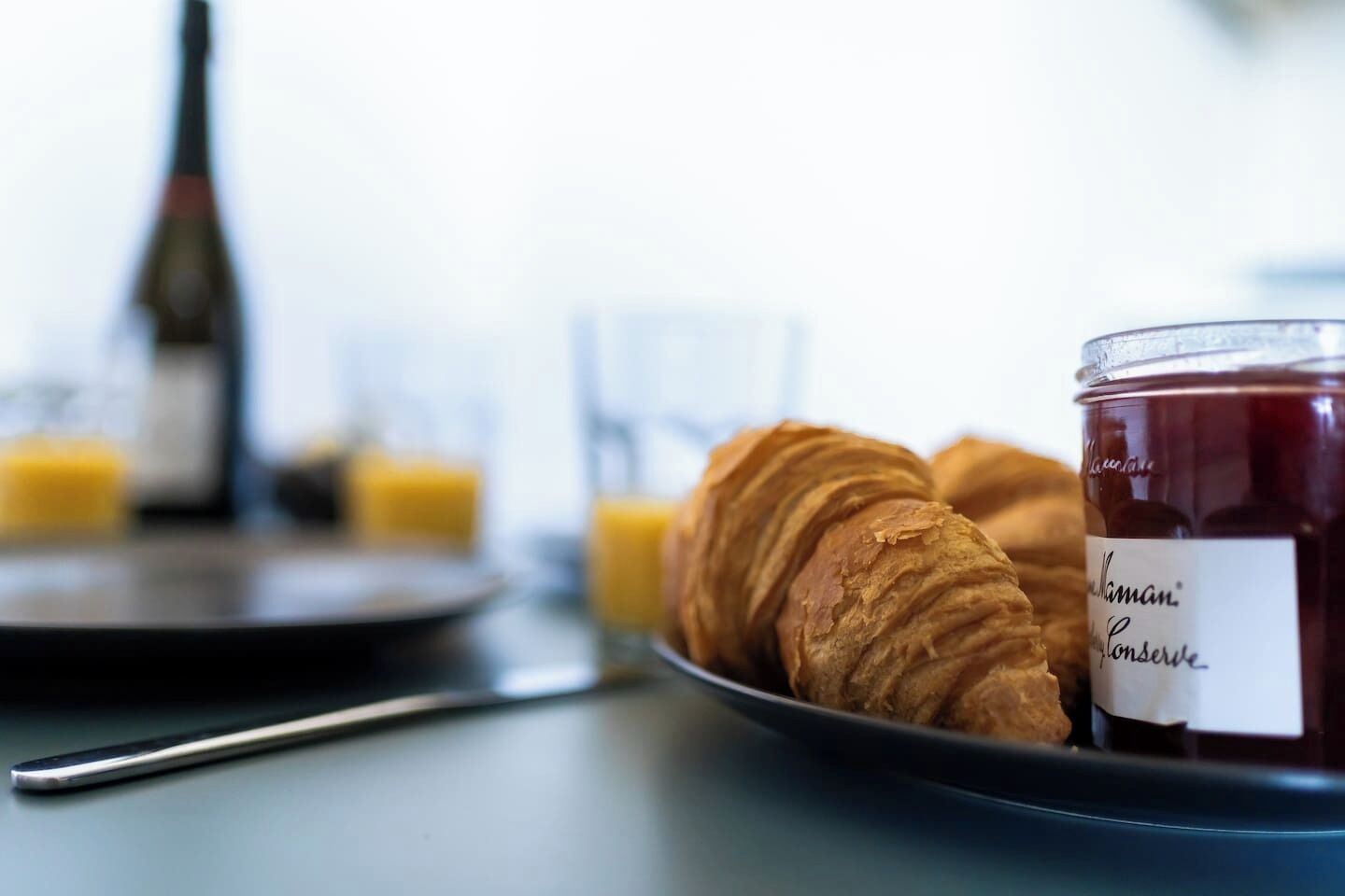 Ein Frühstückstisch mit Croissants, Marmeladenglas und einer Orangensaftflasche.