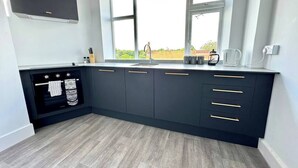 A modern kitchen with dark cabinetry, a built-in oven, and a window providing natural light. - #142 Bournemouth Flat| Near AlumChine Beach|for 10 (Bournemouth)