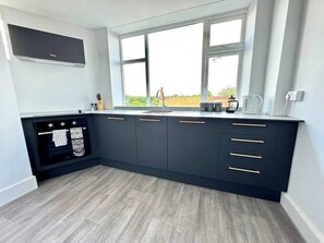 Eine moderne Küche mit dunklen Schränken, einem eingebauten Backofen und einem Fenster, das natürliches Licht hereinlässt.
