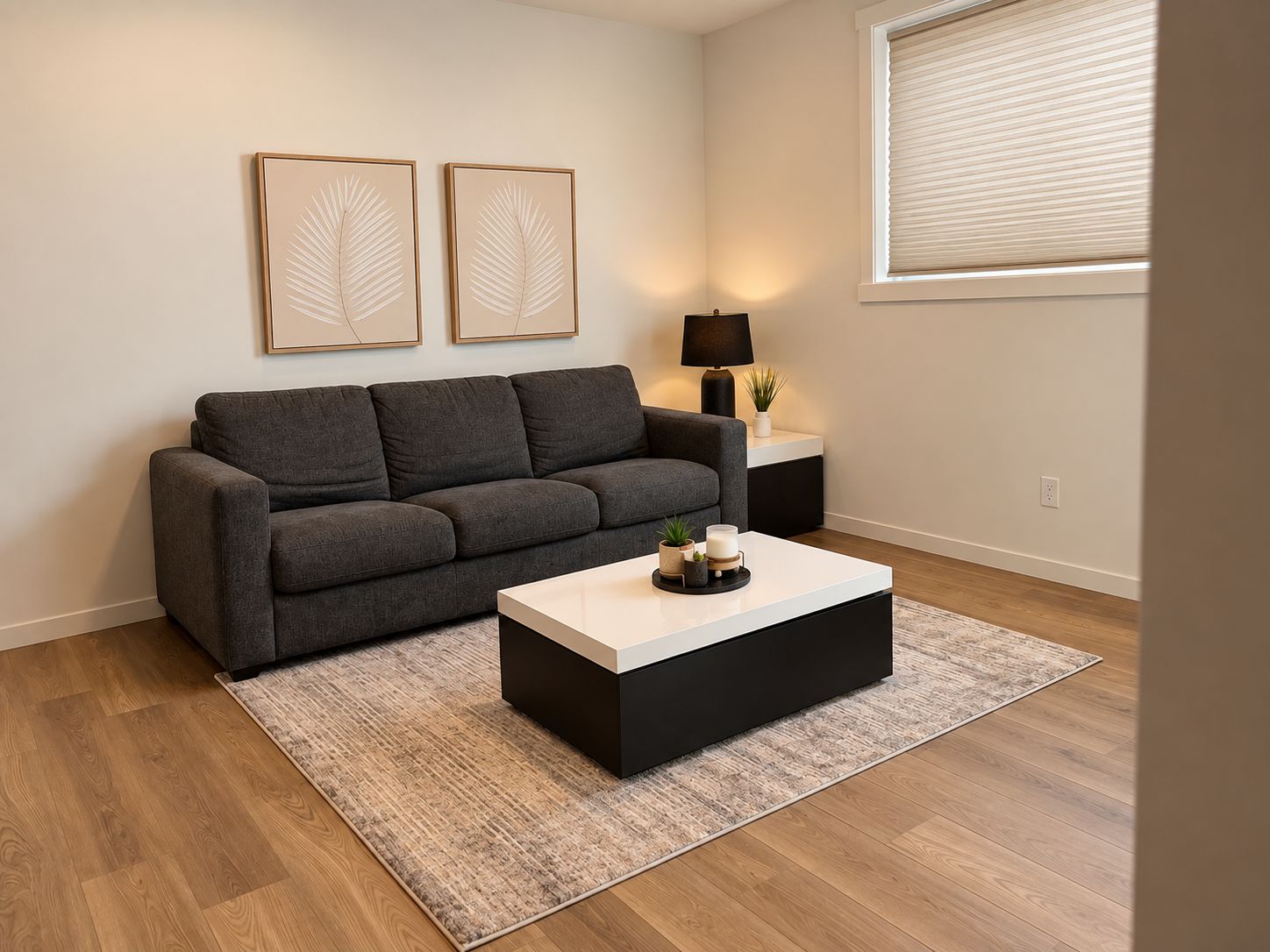 Ein modernes Wohnzimmer mit einem grauen Sofa, einem schwarzen Couchtisch und zwei gerahmten Wandbildern.