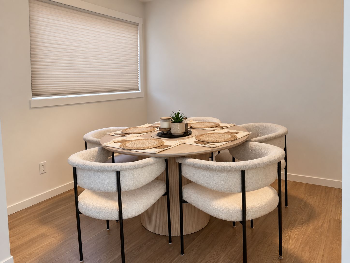 A round dining table with six chairs, a small potted plant, and woven placemats.