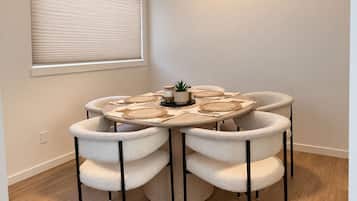 A round dining table with six chairs, a small potted plant, and woven placemats.