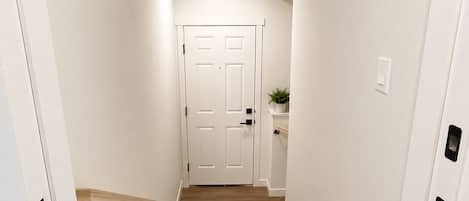 A narrow hallway with a wooden floor, white walls, and a white door at the end.