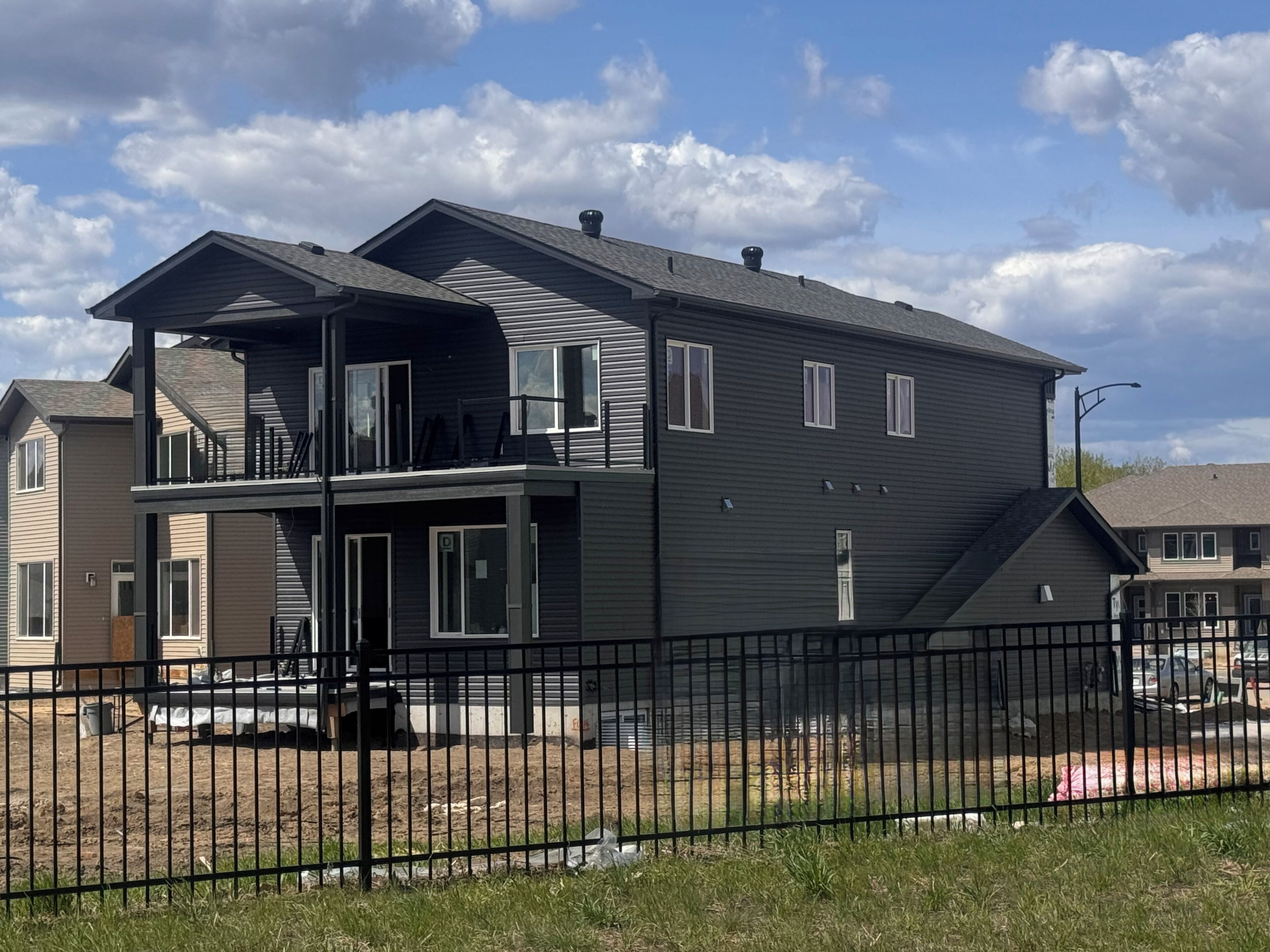 A two-story residential building with a balcony, a fenced yard, and a clear sky.