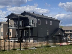 A two-story residential building with a balcony, a fenced yard, and a clear sky.