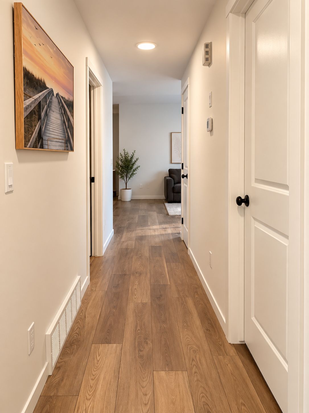 A hallway with wooden flooring, white walls, and a door on the right.