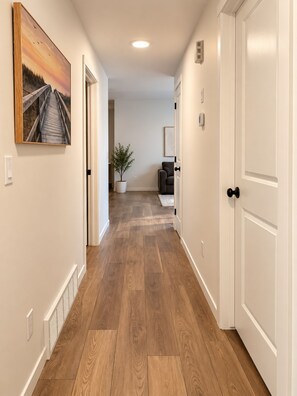 A hallway with wooden flooring, white walls, and a door on the right. - Modern 2BR Retreat | King Bed | Heated Bath Floors (Edmonton)
