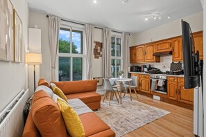 Eine moderne Küche mit Holzschränken, ein Essbereich mit Tisch und Stühlen sowie ein Wohnzimmer mit Sofa und Teppich.