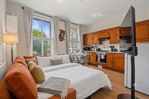 Ein modernes Schlafzimmer mit einem großen Bett, einer Sitzecke mit Tisch und Stühlen sowie einer Küche mit Holzschränken und Geräten.