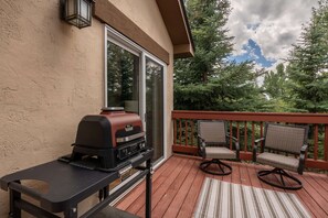 A barbecue grill on a wooden deck with a glass door and a view of trees. - Cascades at EagleRidge Stuart 4 | Hot Tub | AC | Walk to Resort (Steamboat Springs)