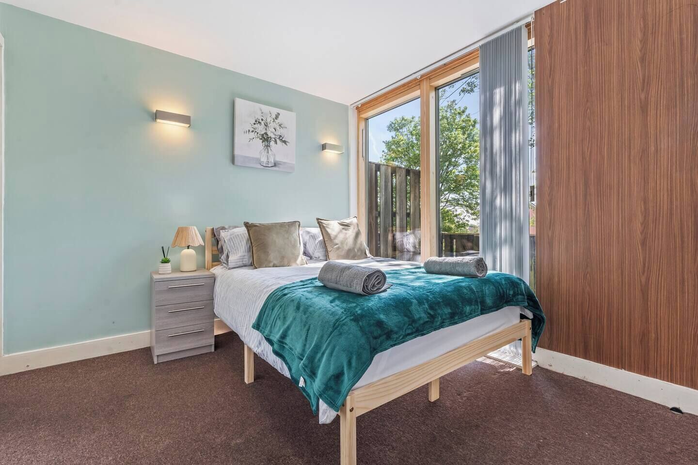 A bedroom with a bed, bedside table, lamp, and a painting on the wall.