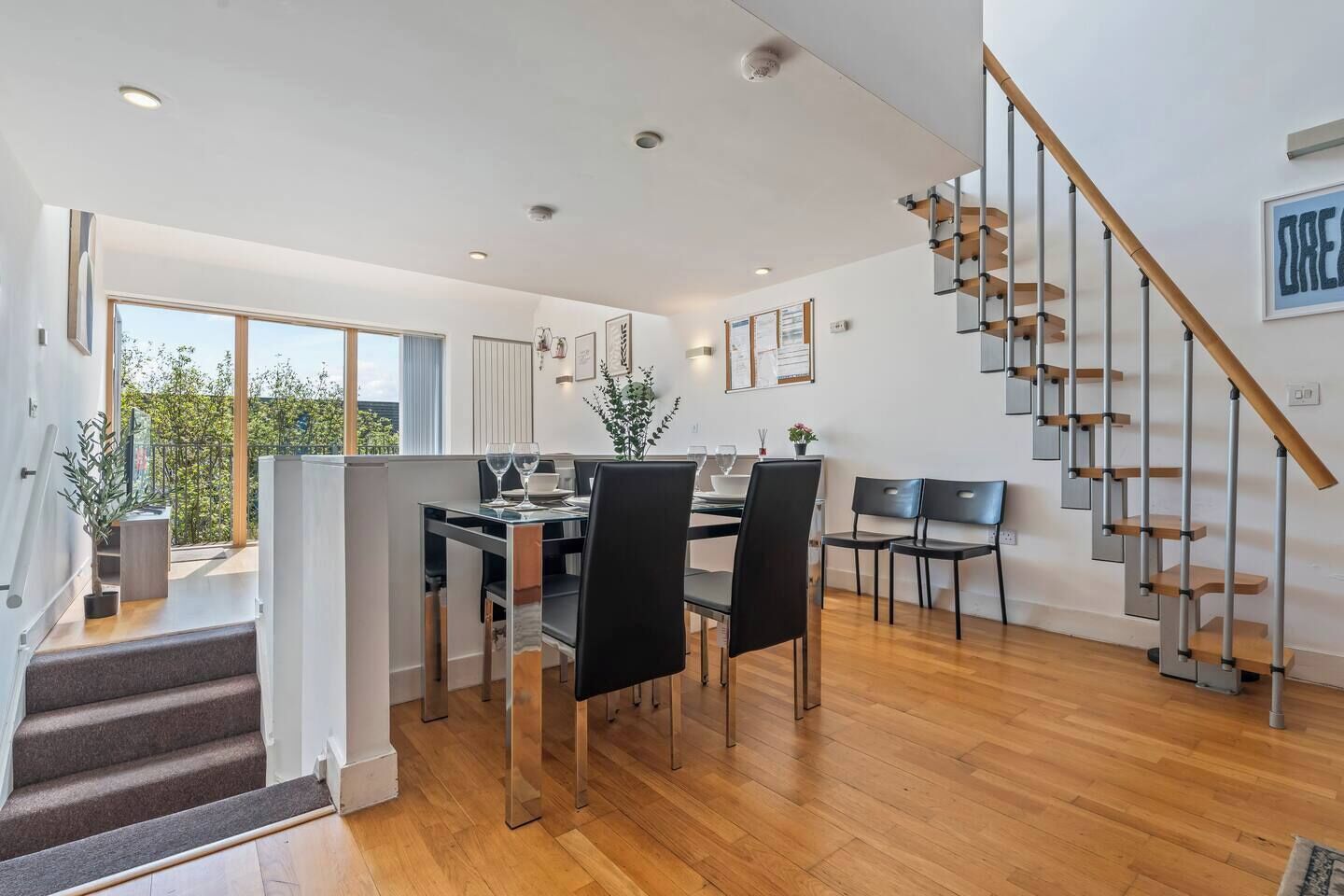 A modern interior with a dining area, staircase, and a view to the outside.