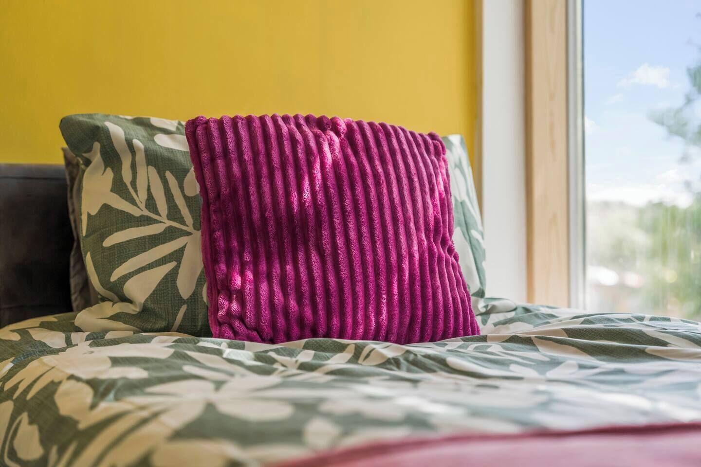 A bed with a patterned bedspread and a pillow with a leaf design.