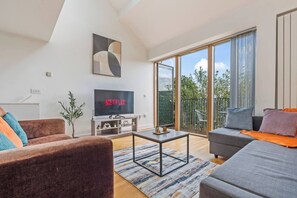 Uma sala de estar moderna com televisão de tela plana, um sofá, uma mesa de centro e uma varanda com vista para o verde.
