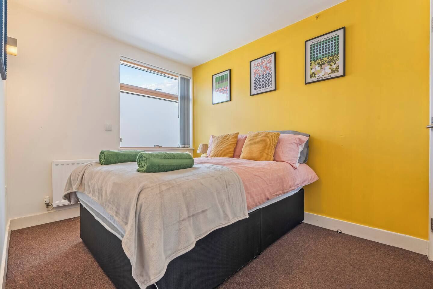 A bedroom with a bed, a window, and three framed artworks on the wall.