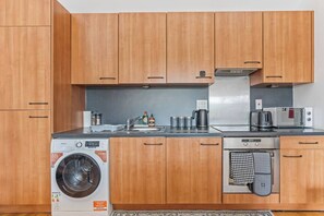 Een functionele keuken met houten kastjes, een geïntegreerde wasmachine, een broodrooster en een waterkoker.