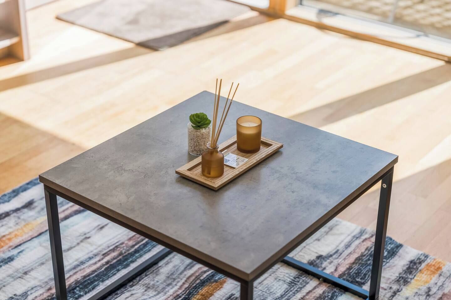 A square table with a metal frame, a small plant, and two candles on a tray.