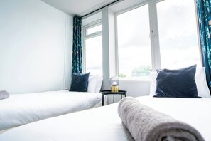 A hotel room with two beds, a nightstand, and a window with curtains. - #159 Sunny Stay Near the Bournemouth Beach -For 9 (Bournemouth)
