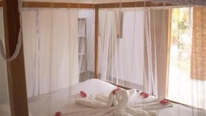 A four-poster bed with white linens and pink flowers, a ceiling fan, and a window with curtains. - finca montania sagrada Ometepe (Mérida)