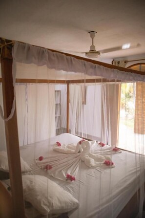 A four-poster bed with white linens and pink flowers, a ceiling fan, and a window with curtains. - finca montania sagrada Ometepe (Mérida)