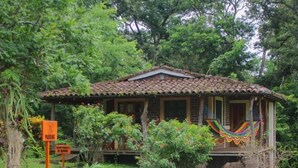 A rustic wooden house with a tiled roof, surrounded by greenery and rocks. - finca montania sagrada Ometepe (Mérida)