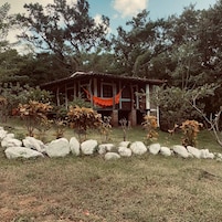 Una casa rústica con porche, rodeada por un muro de piedra y abundante vegetación.