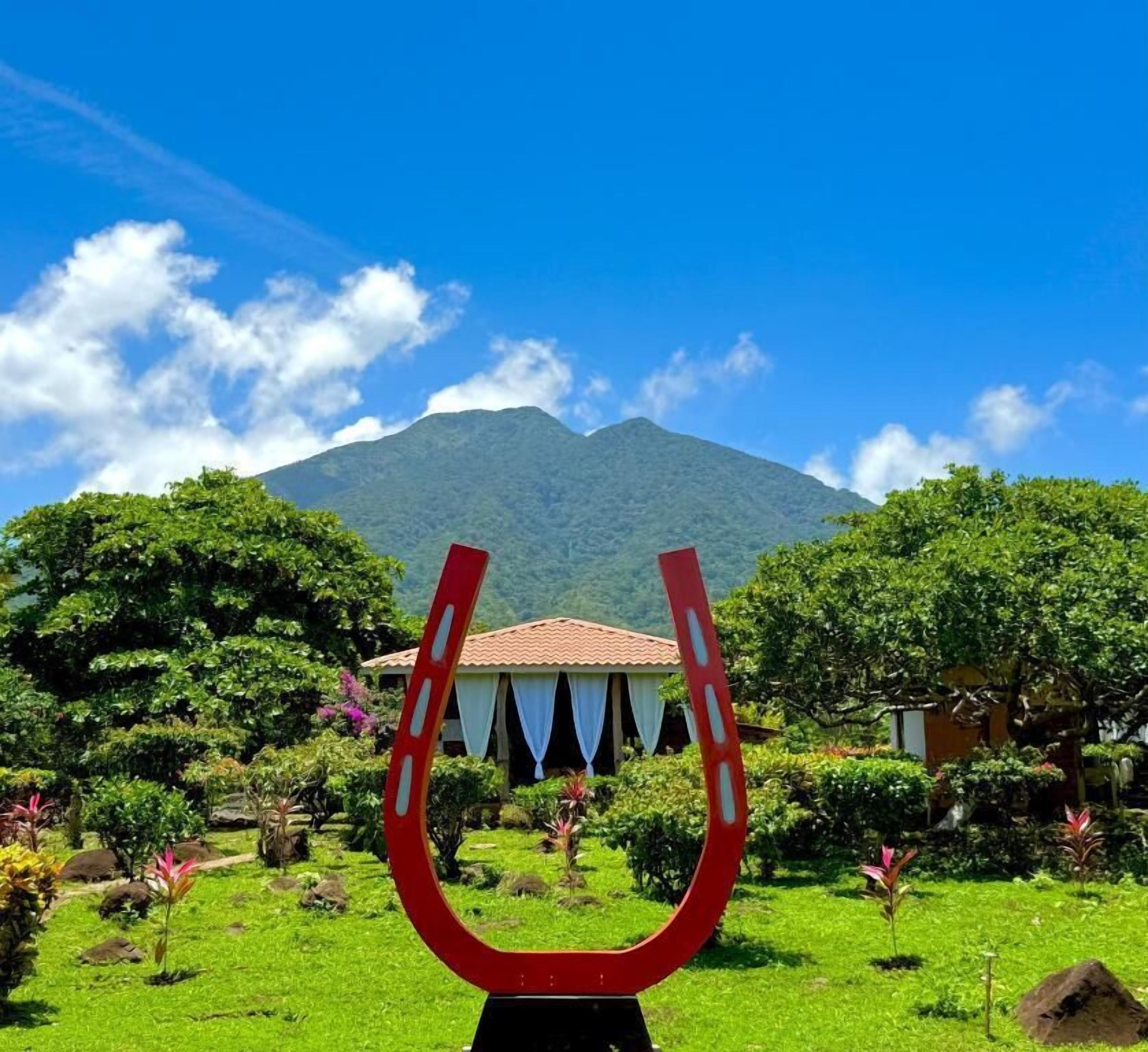 Une sculpture en forme de fer à cheval dans un jardin, avec une montagne en arrière-plan.