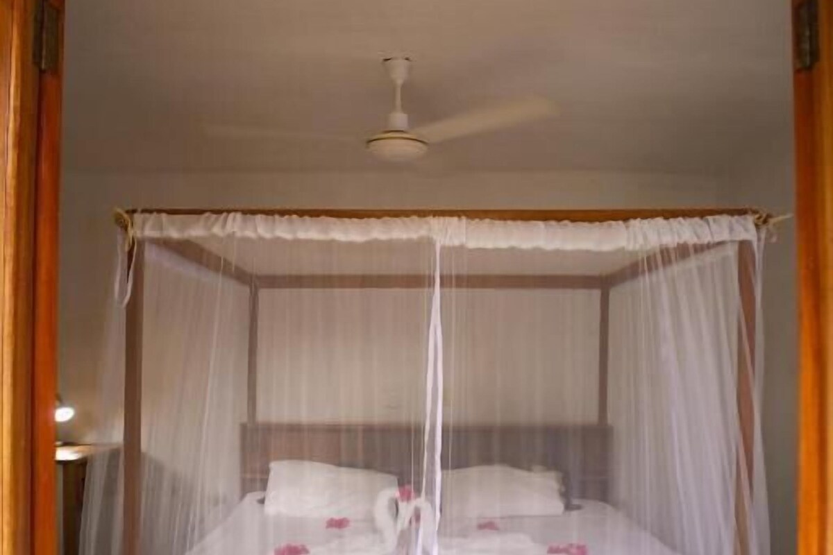 A bed with a canopy, a ceiling fan, and a stone floor.