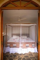 Uma cama com dossel, um ventilador de teto e piso de pedra.
