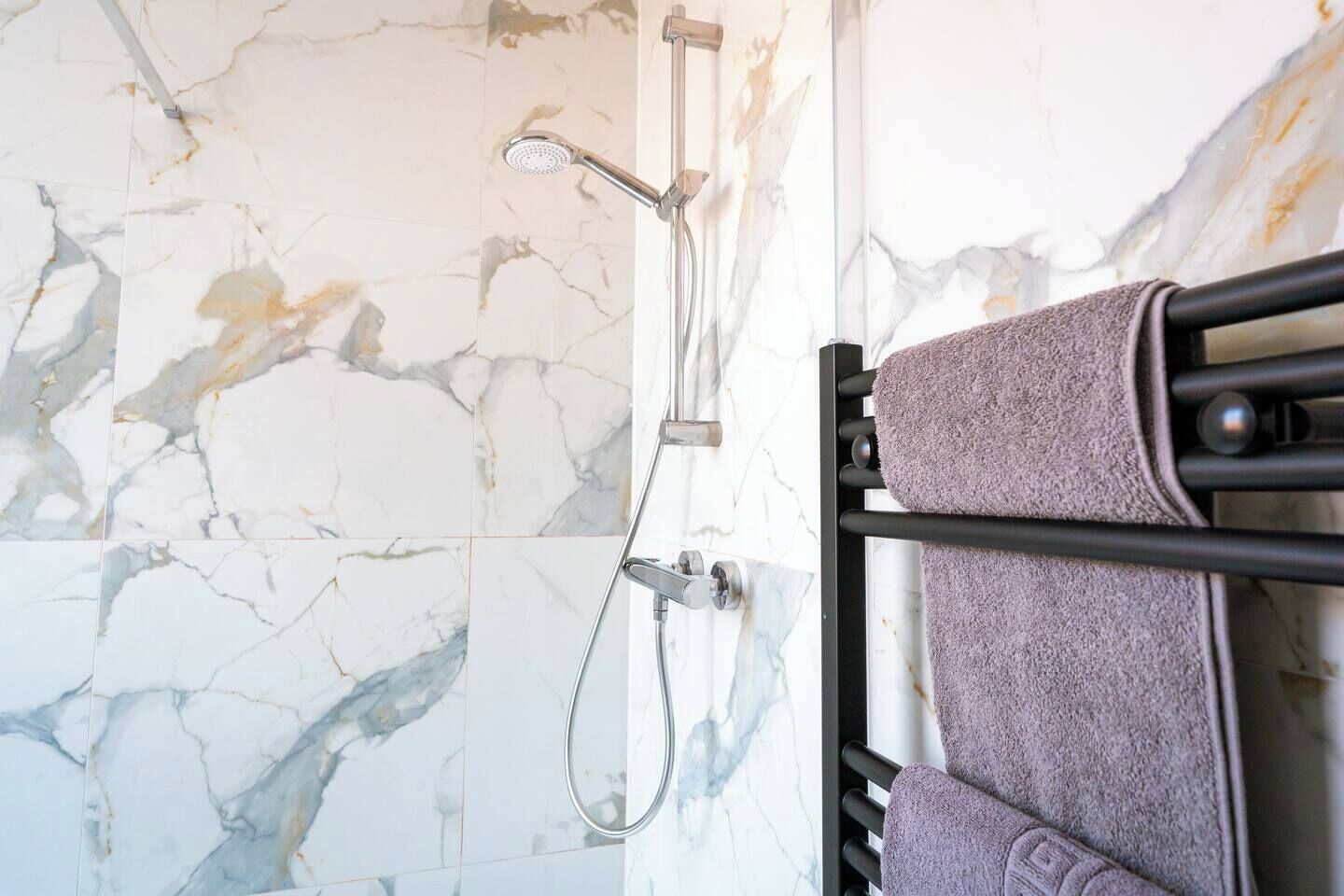 Een badkamer met een marmeren wand, een douche met een handdouche en een handdoekhouder met twee handdoeken.