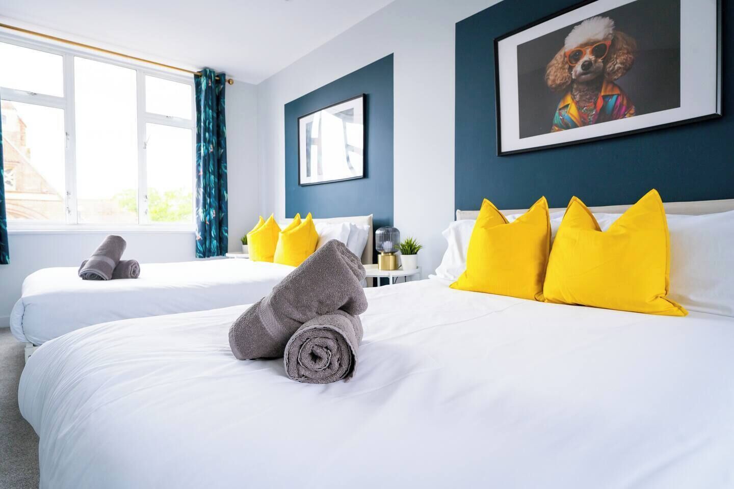 Een hotelkamer met twee bedden, een groot raam en een ingelijst schilderij aan de muur.