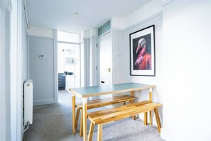 A modern interior with a wooden dining table and bench, a framed artwork on the wall, and a kitchen area in the background. - #158 Cozy Flat Near Bournemouth Beach - Sleeps 10 (Bournemouth)