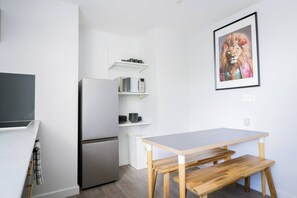 A compact kitchen with a refrigerator, microwave, and a small dining table with benches. - #158 Cozy Flat Near Bournemouth Beach - Sleeps 10 (Bournemouth)