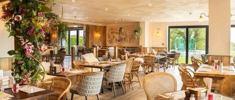 A restaurant with wicker furniture, large windows, and a view of greenery outside.
