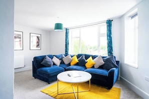 Ein Wohnzimmer mit einem blauen Sofa, einem runden Couchtisch und einem gelben Teppich.