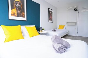 A hotel room with two beds, bright yellow pillows, a rolled towel, a framed picture on the wall, and a white wardrobe. - #158 Cozy Flat Near Bournemouth Beach - Sleeps 10 (Bournemouth)