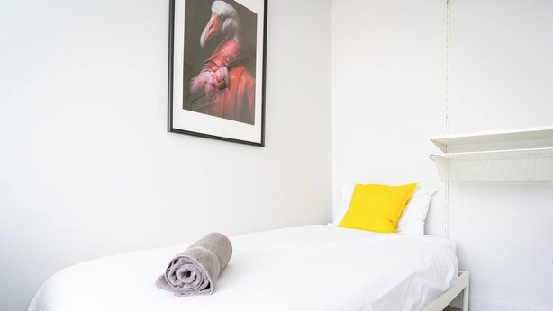A single bed with a rolled towel, a bright yellow pillow, and a framed picture on the wall. - #158 Cozy Flat Near Bournemouth Beach - Sleeps 10 (Bournemouth)
